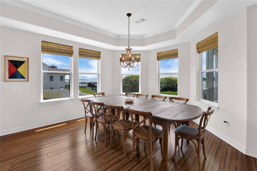 This dining area features a spacious wooden table with seating for eight, set on hardwood floors. Large windows provide ample natural light and offer scenic views, complemented by a stylish chandelier.