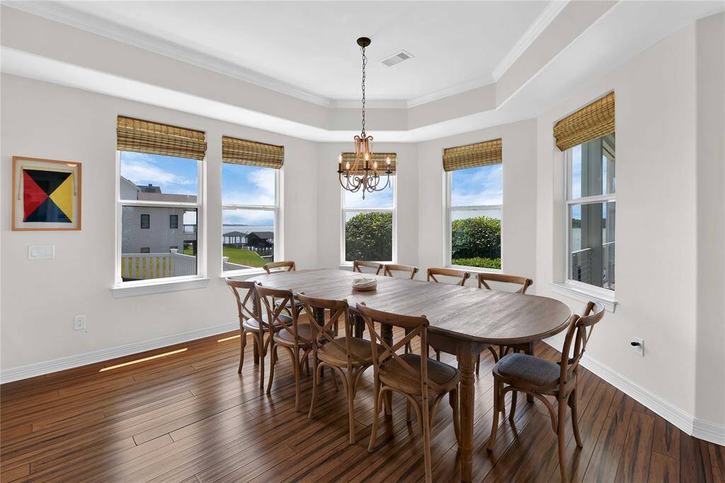 Bright dining area with large windows offering scenic views, hardwood floors, and a rustic chandelier above a wooden table.