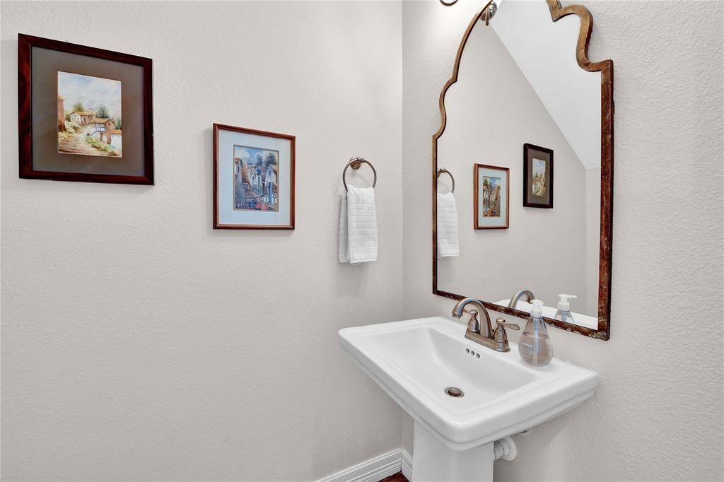 This bathroom features a stylish pedestal sink with bronze fixtures, complemented by a large decorative mirror. The neutral wall color is enhanced by two framed artworks and a hand towel ring.