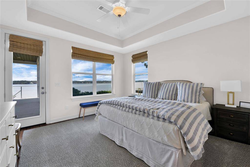 This bedroom offers stunning lake views, featuring large windows and a door leading to a deck. It has a spacious layout with a cozy bed and neutral decor, perfect for relaxation.