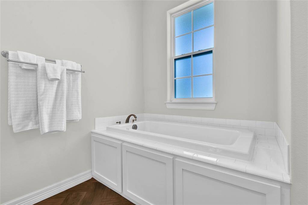 This bathroom features a clean, white bathtub with an elegant tile surround and a frosted window for natural light. It includes a towel rack with neatly arranged towels, creating a bright and inviting space.