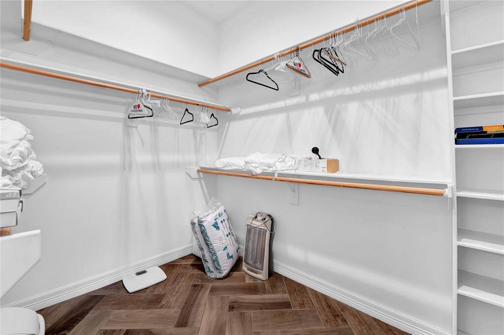 This is a spacious walk-in closet featuring white walls, ample hanging space with wooden rods, and built-in shelving. The floor has a herringbone pattern, adding a touch of elegance.
