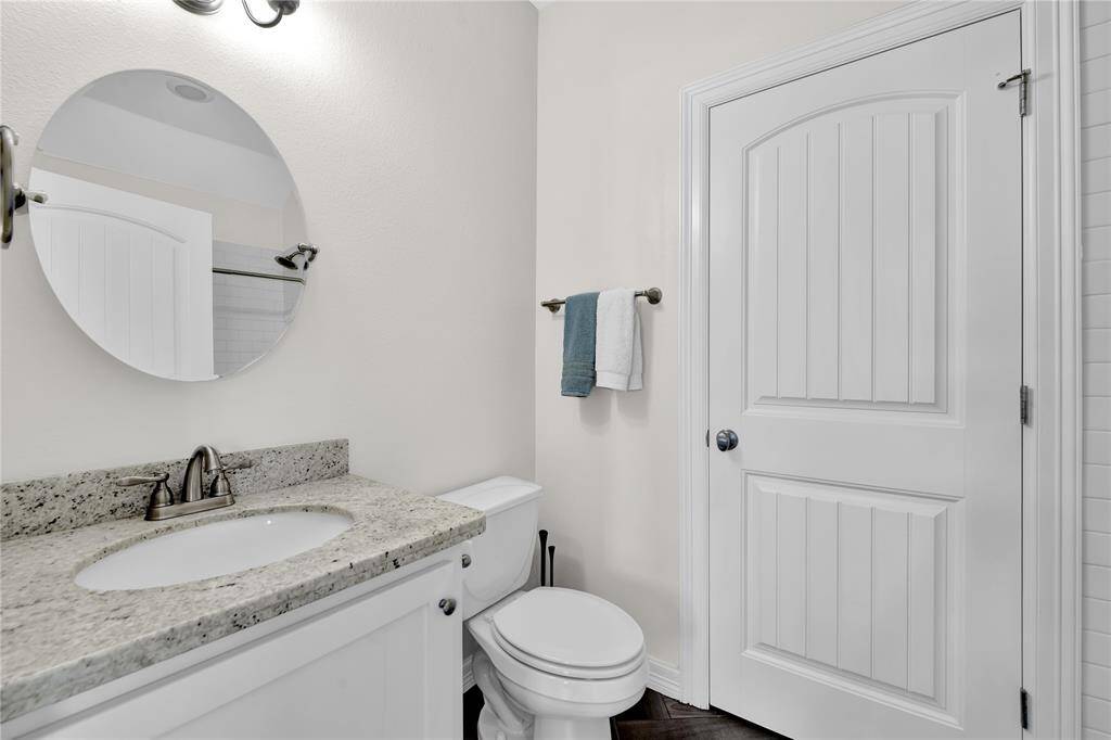 This is a modern bathroom featuring a granite countertop with an undermount sink, a round mirror, and a white paneled door. The space has neutral walls and a towel rack, creating a clean and fresh look.