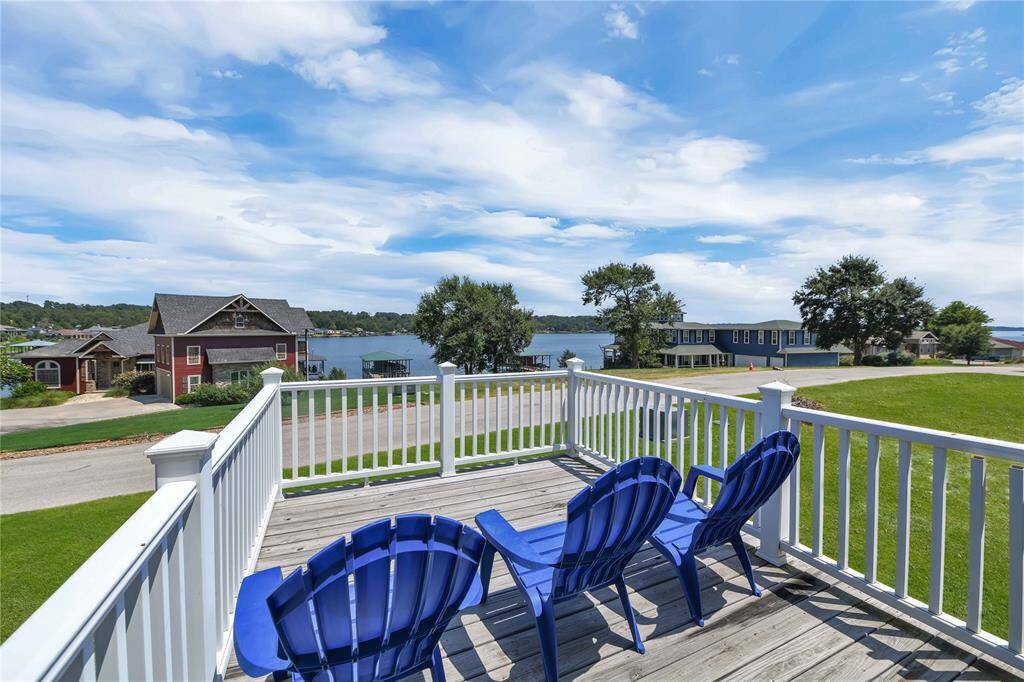 This photo showcases a spacious deck with blue chairs overlooking a serene lake view. The area is surrounded by lush greenery and charming homes, creating a peaceful and picturesque setting. Perfect for relaxation and enjoying scenic vistas.