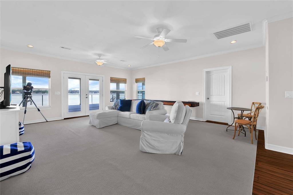 This spacious living room features large windows and French doors offering stunning water views. It has a neutral color palette, ceiling fans, and comfortable seating. The room also includes a telescope for stargazing and a cozy seating area for relaxation.