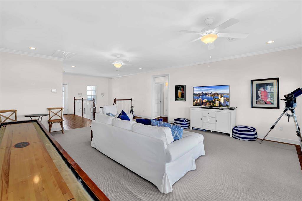 This spacious living room features a cozy seating area with a white sofa, a large TV, and decorative art on the walls. The room is bright with natural light, thanks to large windows, and includes amenities like a shuffleboard table and a telescope, providing a family-friendly, entertaining space.