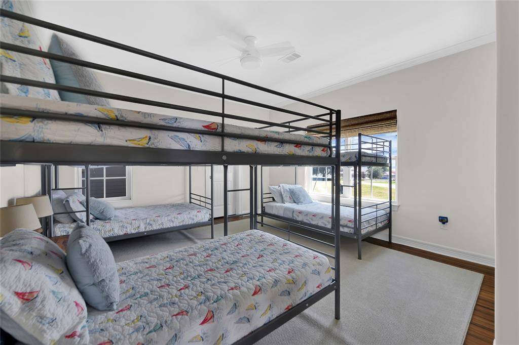 This bright bedroom features three metal bunk beds with playful bedding, ample natural light from large windows, and hardwood floors, offering a cozy and functional space for multiple occupants.