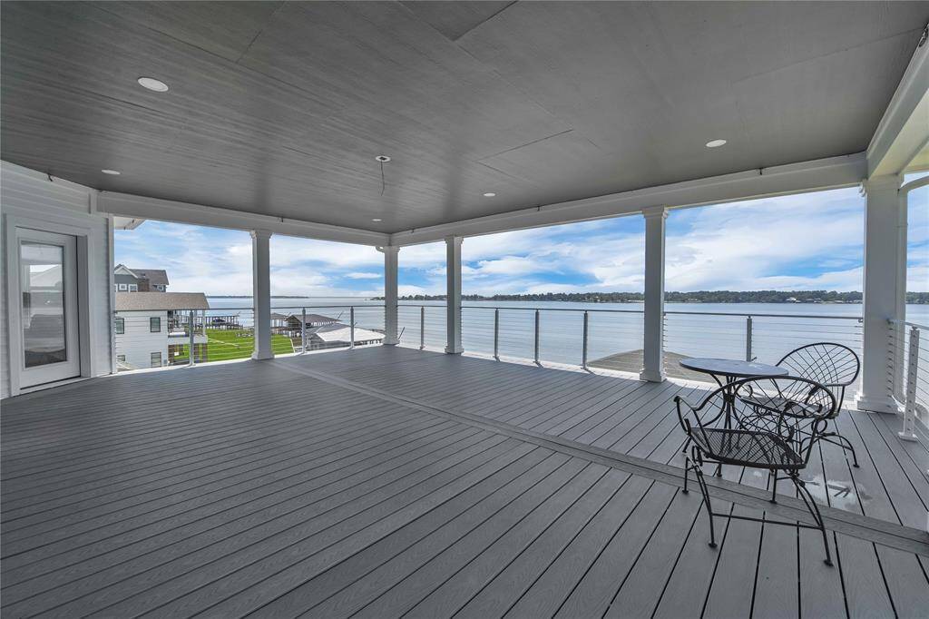 This spacious covered deck offers stunning waterfront views, featuring a sleek railing and ample space for outdoor seating. Perfect for relaxing or entertaining while enjoying the serene lake scenery.