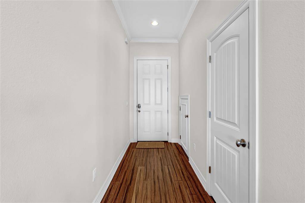 This hallway features light-colored walls, hardwood flooring, and a white front door. It includes a closet door on the right and recessed lighting, creating a bright and welcoming entrance.