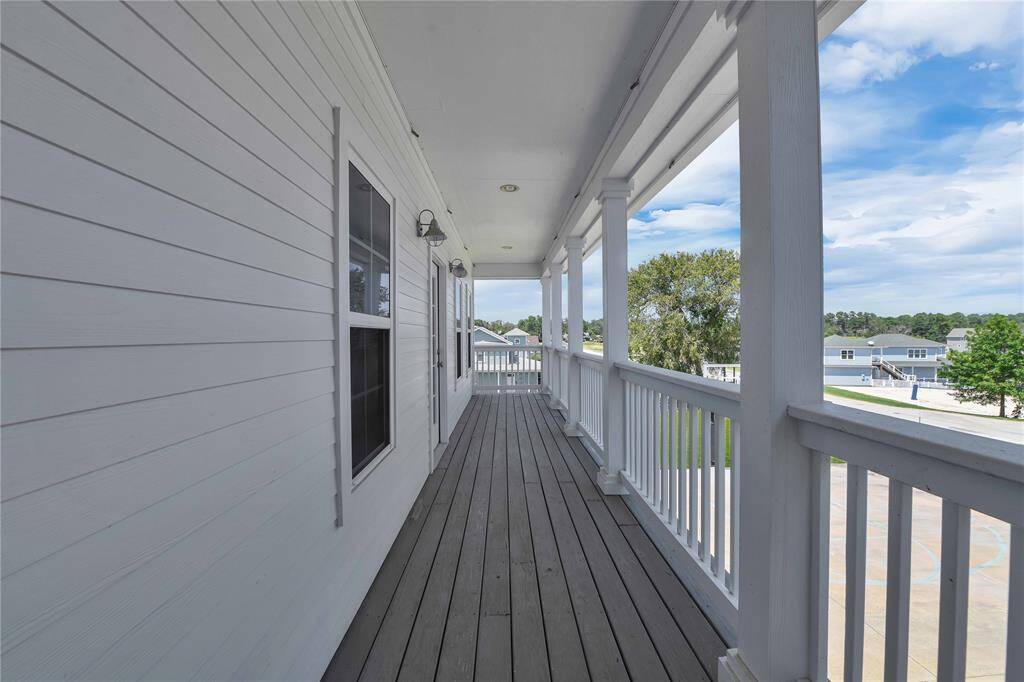 This photo showcases a spacious, covered porch with wood flooring and white railings, offering a peaceful view of a residential neighborhood. Ideal for enjoying the outdoors or relaxing in the evening.
