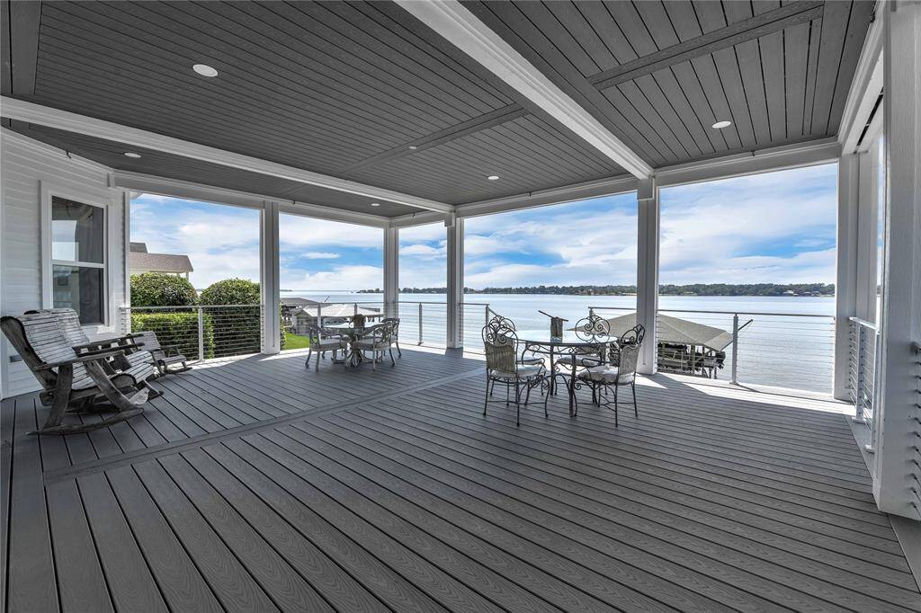 This photo showcases a spacious, covered deck with elegant outdoor seating and rocking chairs, offering stunning views of the water. The area is perfect for relaxation and entertaining, featuring a stylish wooden floor and ceiling.