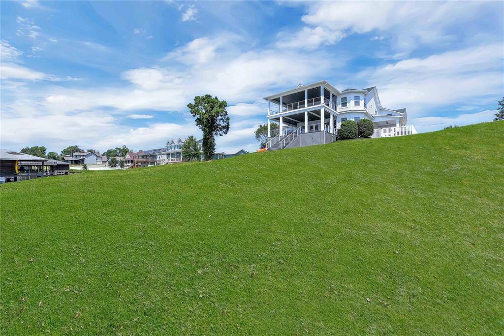 This photo showcases a modern, multi-story home on a spacious, sloped lawn. The house features large windows and a porch, offering expansive views. The surrounding area appears to be a well-maintained neighborhood with other similar homes.