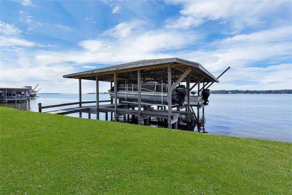 This photo showcases a serene waterfront view with a boat docked under a covered lift, surrounded by lush green grass and a calm, expansive body of water. Ideal for boating enthusiasts seeking a peaceful lakeside lifestyle.