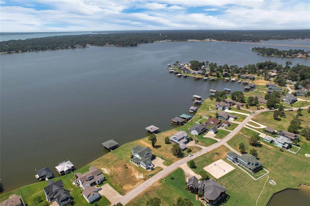 This aerial photo showcases a picturesque lakeside community with homes featuring direct water access. The area is surrounded by lush greenery and offers serene views of the expansive lake, making it an ideal location for waterfront living.
