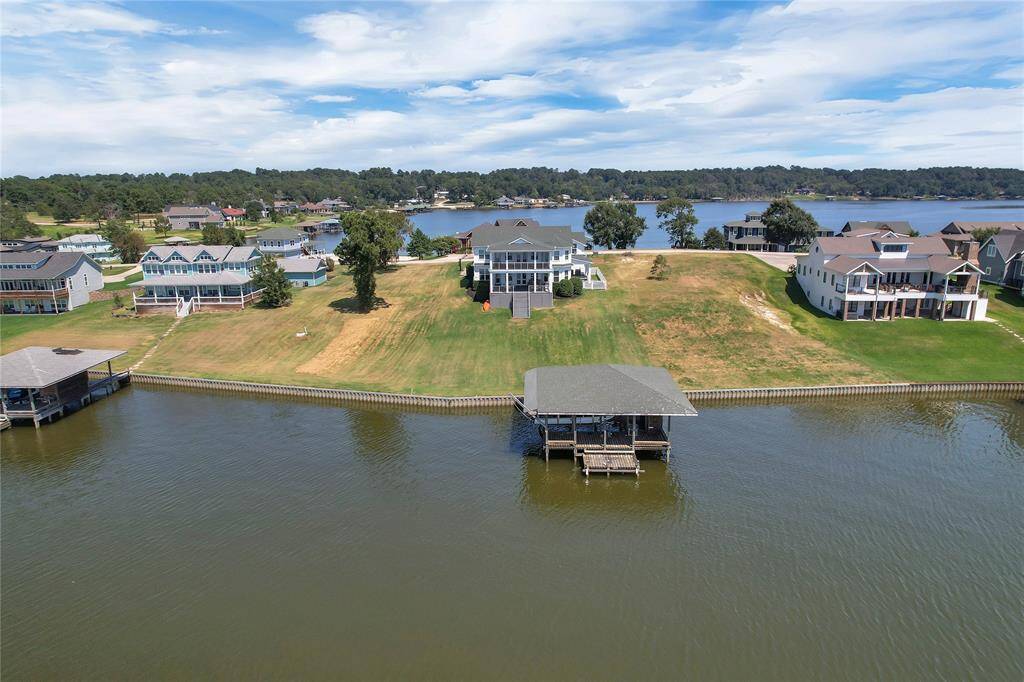 This photo showcases a spacious waterfront property with a modern house, large lawn, and a private boat dock, offering serene lake views and a peaceful neighborhood setting.