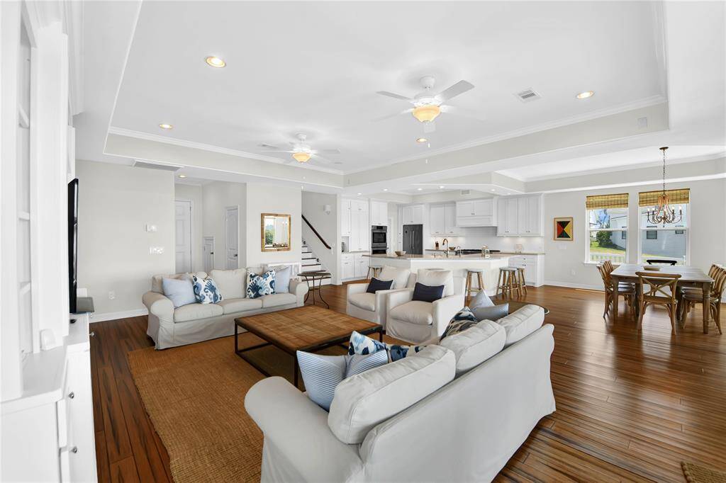 This photo showcases a spacious open-concept living area with hardwood floors, featuring a cozy seating arrangement, a modern kitchen with a large island and bar seating, and a bright dining area. The room is well-lit with natural light and recessed lighting, creating a welcoming atmosphere.