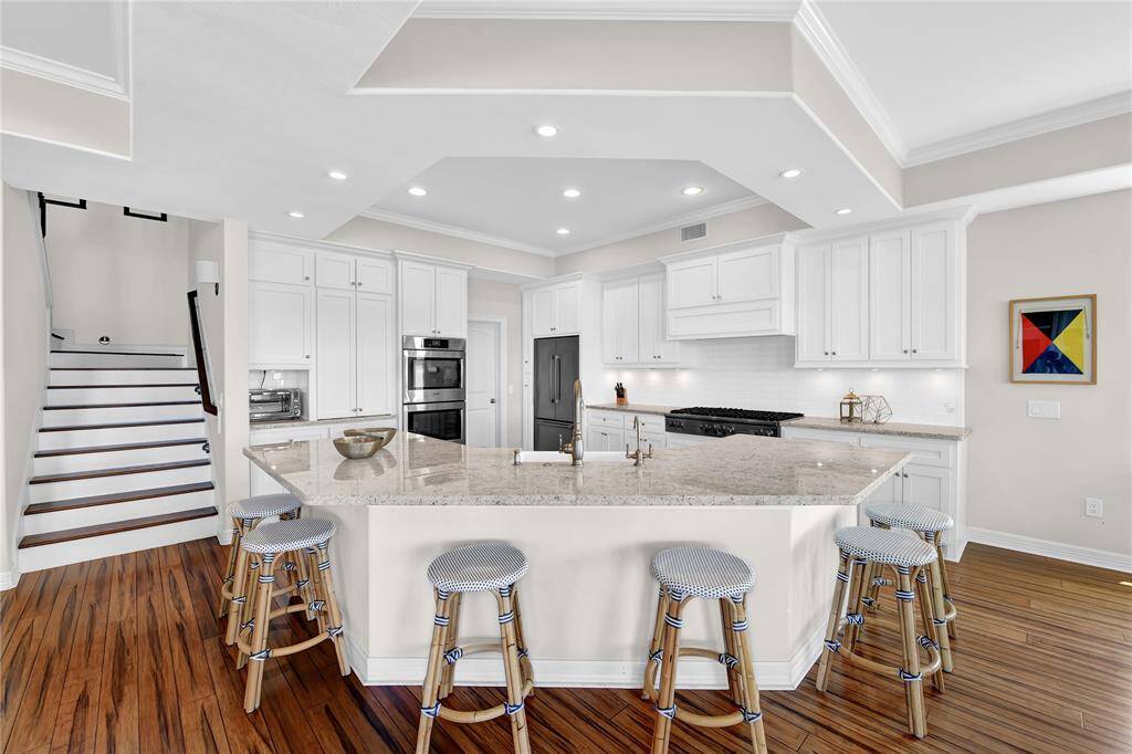 This modern kitchen features a spacious island with granite countertops, seating for five, and ample cabinetry. It includes stainless steel appliances, recessed lighting, and hardwood floors, creating a bright and inviting space.