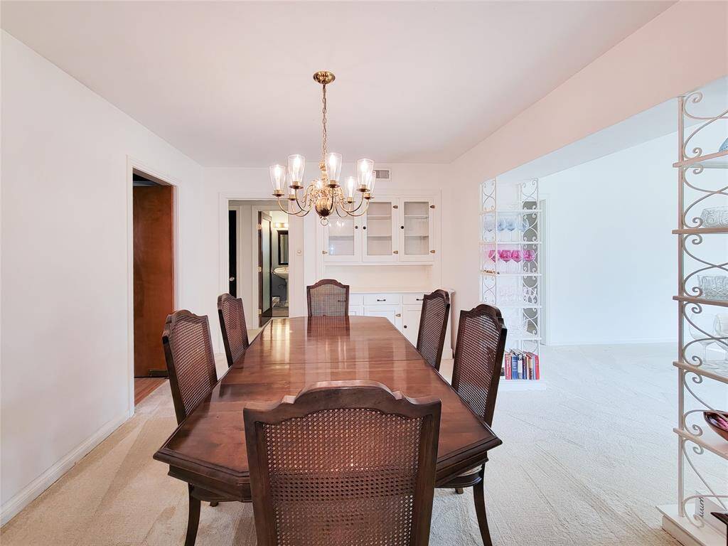 This photo showcases a cozy dining room with a classic wooden table and chairs under an elegant chandelier. It features built-in cabinets and connects to a bright living room through a decorative opening.
