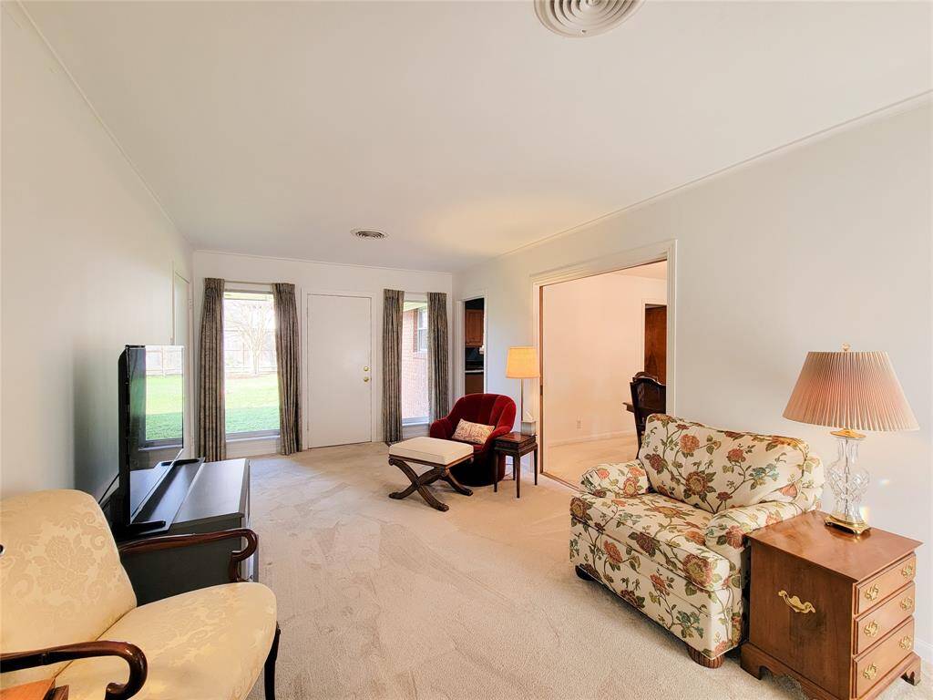 Bright home office with natural light, featuring large windows with curtains, neutral carpet, and elegant furniture including a desk and chairs. Cozy and inviting space for work or study.