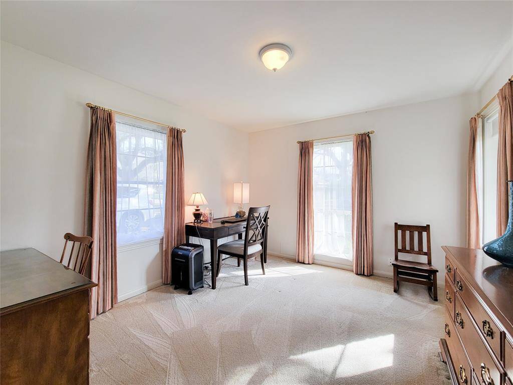 This bright room features neutral walls and carpet, with three large windows providing ample natural light, and there's space for a small desk or seating area, ideal for a home office.