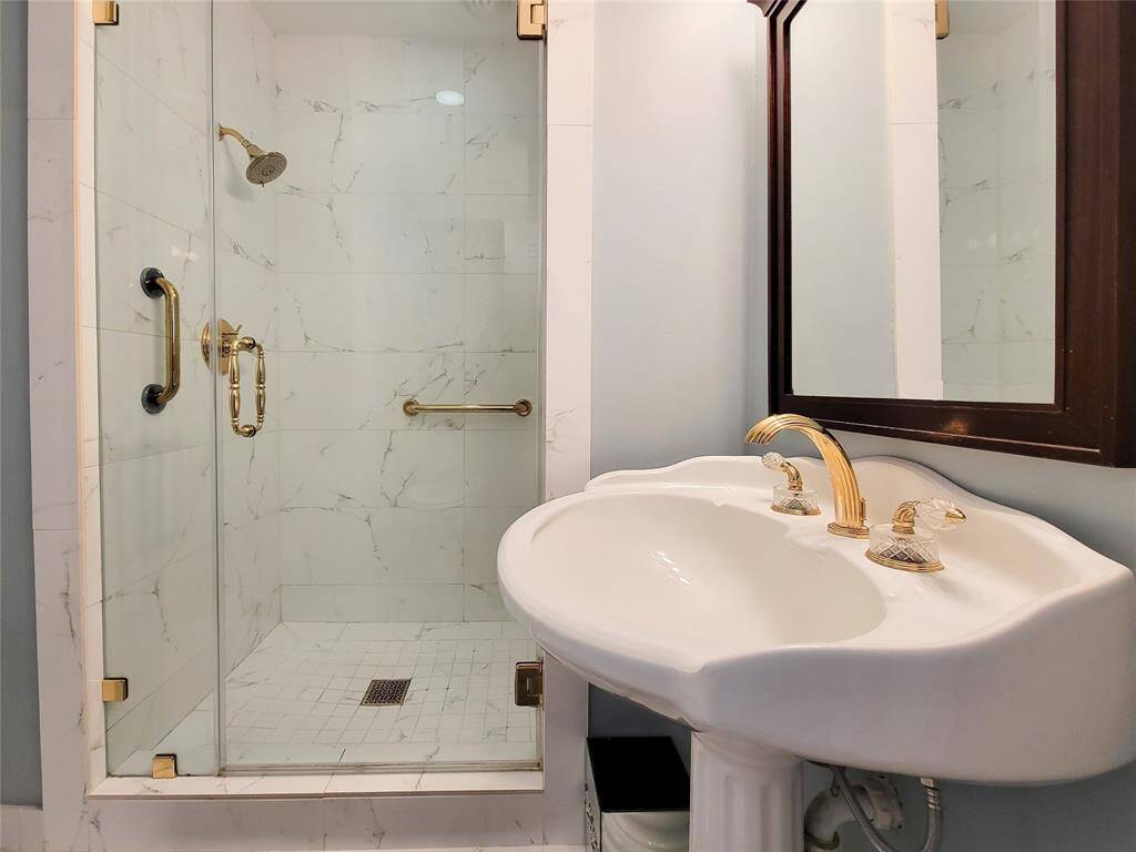 This bathroom features a frosted glass door, pedestal sink, and modern lighting. It has a light blue color scheme with a window, and a neatly arranged towel rack, creating a clean, bright, and inviting space.