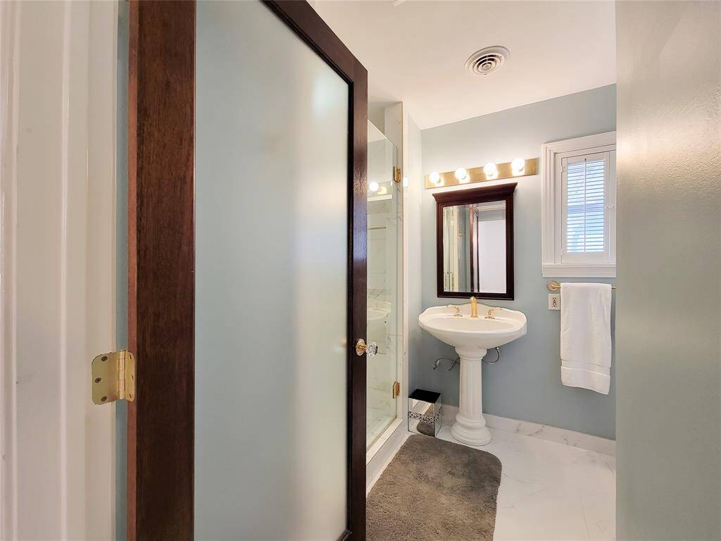 Frosted door leading to remodeled bathroom with glass enclosed shower with seating ledge and pedestal sink.