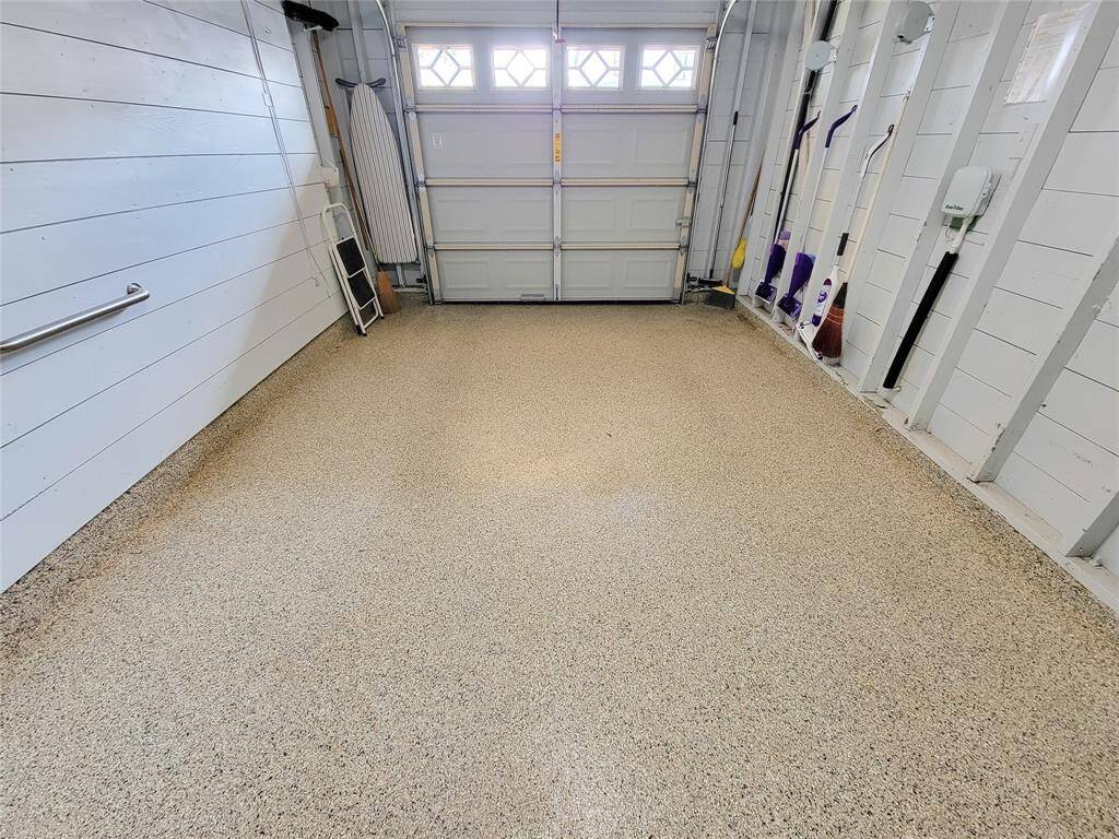 This photo shows a spacious, well-lit garage with white paneled walls and a speckled floor. It features wall-mounted storage hooks, cabinets for additional storage, and a fire extinguisher for safety. There is a door leading to another area, adding convenience and functionality.