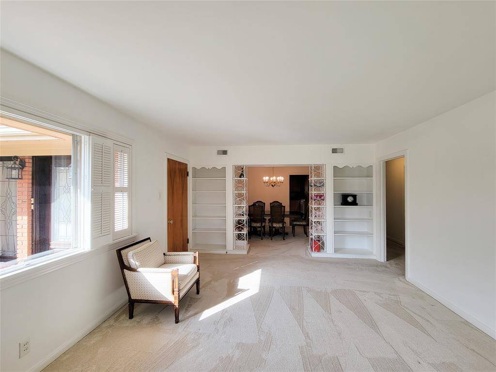 This photo showcases a bright and spacious living area with large windows, neutral carpeting, and built-in shelving. It opens into a dining room with a chandelier, creating a seamless flow between spaces.