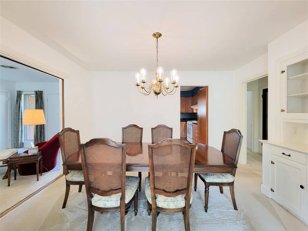 Alternate view of this spacious dining room. A classic chandelier provides lighting, and built-in cabinetry offers storage. The room features light-colored walls and carpet, with decorative metal dividers adding a touch of charm.
