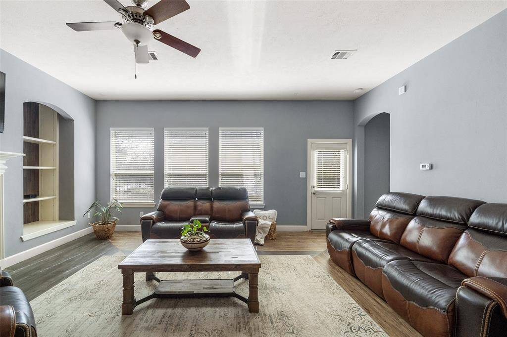 This living room features a cozy and modern design with gray walls and ample natural light streaming through three large windows.