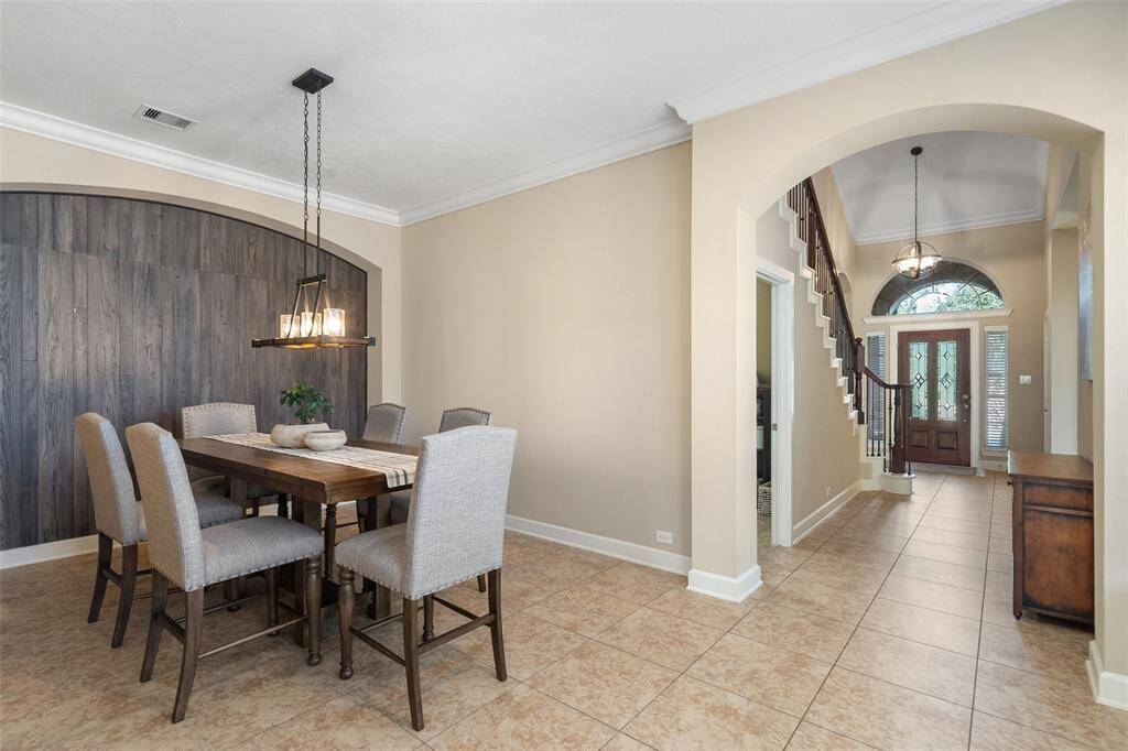 This inviting home features an elegant dining area with a rustic wood accent wall and a stylish chandelier. Adjacent to the dining space is an open foyer with high ceilings, arched entryways, and a staircase leading to the upper level. The entryway is brightened by a large window above the front door, creating a welcoming atmosphere.