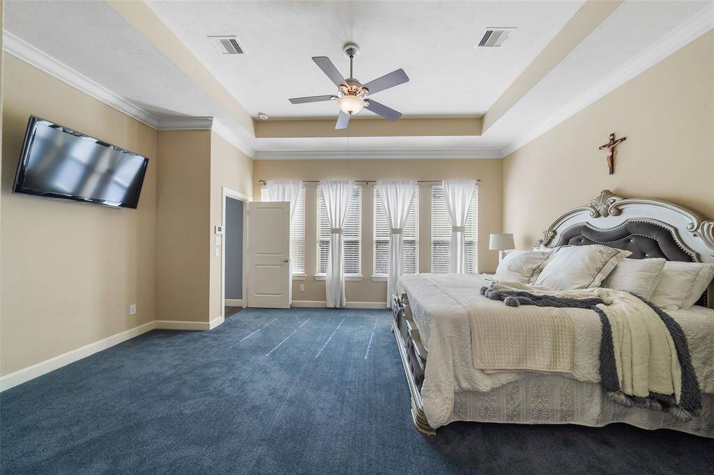 Spacious bedroom with a cozy atmosphere with ample natural light from multiple windows. The room has elegant crown molding and a tray ceiling