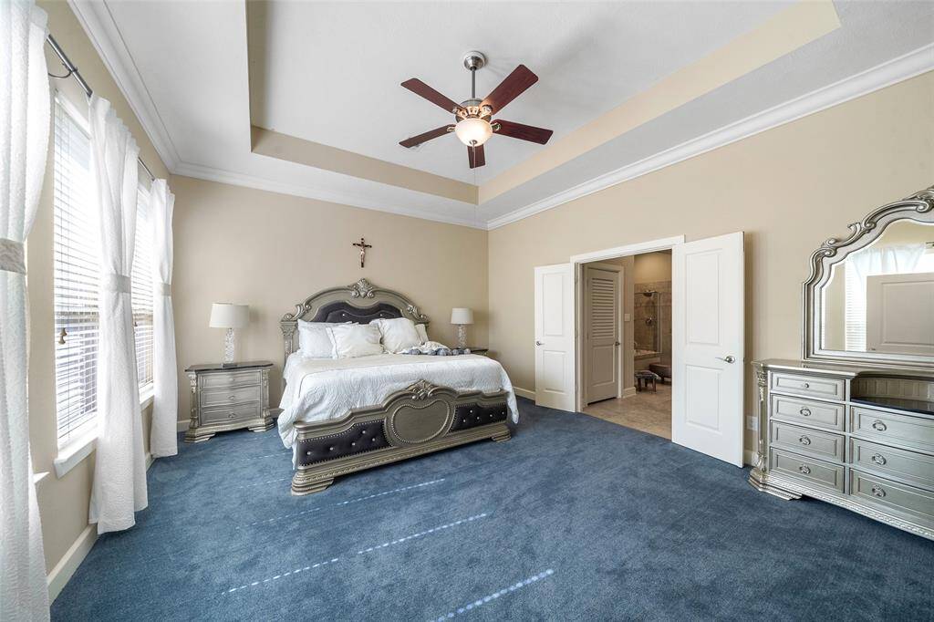 This spacious bedroom features a tray ceiling with a ceiling fan, and ample natural light from large windows.