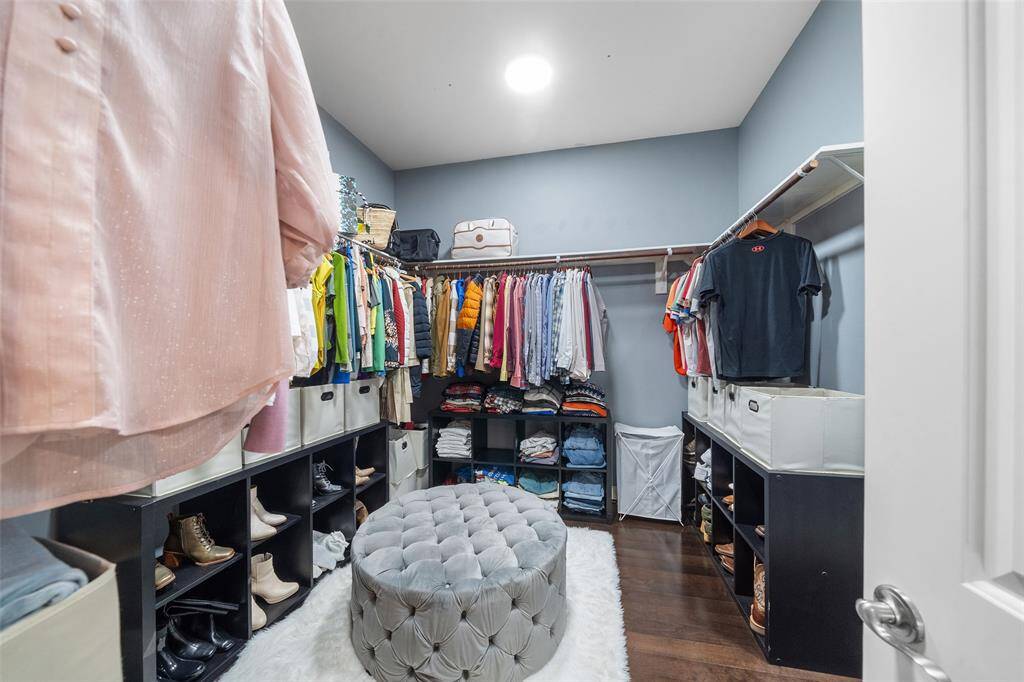 This spacious walk-in closet features ample hanging space, open shelving for shoes and accessories, and a plush ottoman. The room is well-lit with a contemporary design, offering an organized and stylish storage solution.