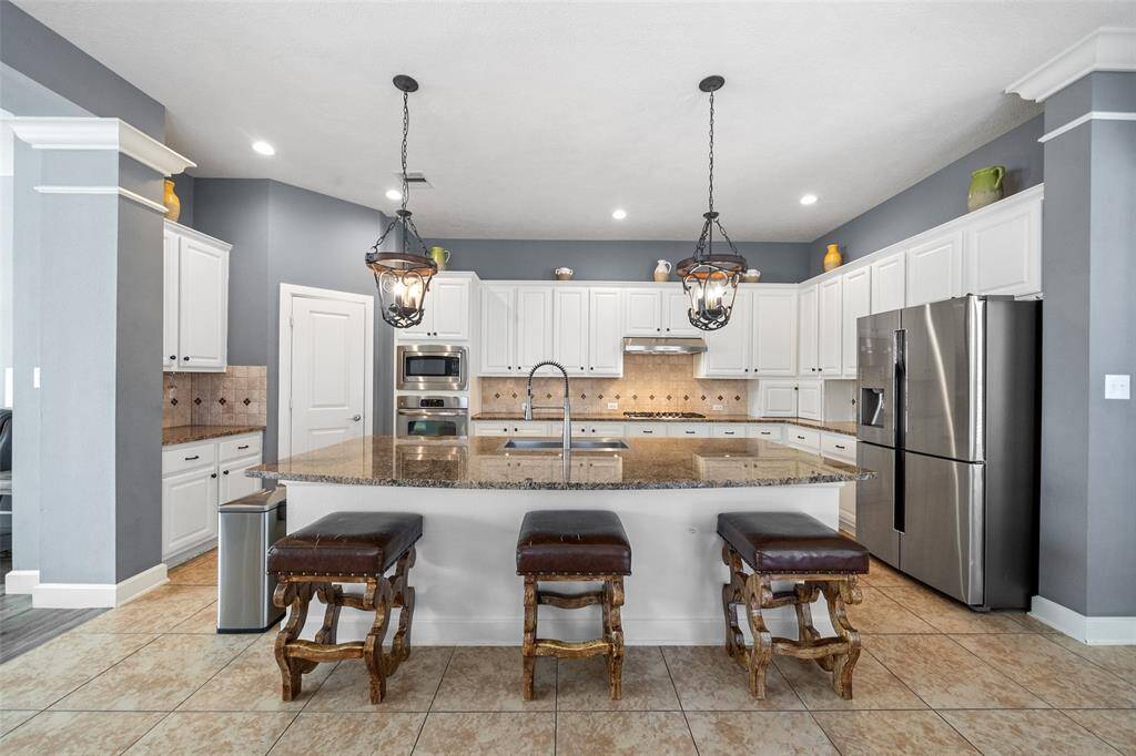 This kitchen features a spacious layout with a large granite island, stainless steel appliances, and elegant pendant lighting. It offers ample cabinet storage, tiled flooring, and a cozy seating area, perfect for family gatherings and entertaining.