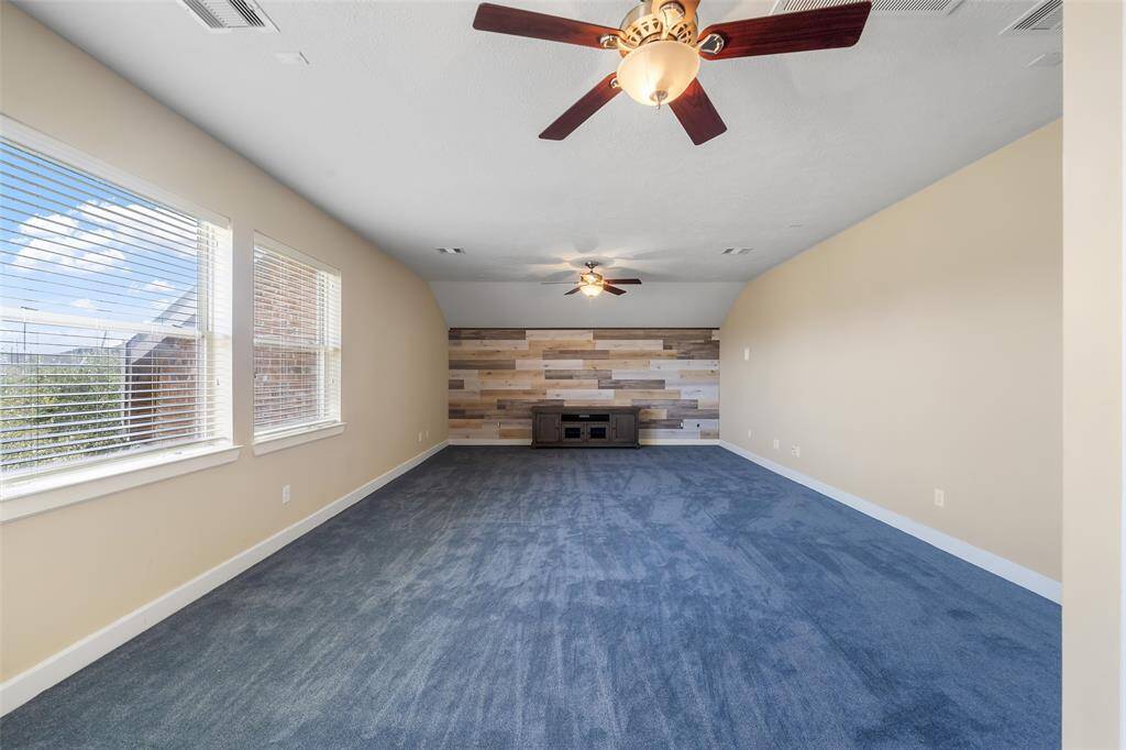 Spacious game room with a full bathroom has large windows providing natural light. Features a unique wood accent wall, ideal for a cozy living area or entertainment space.