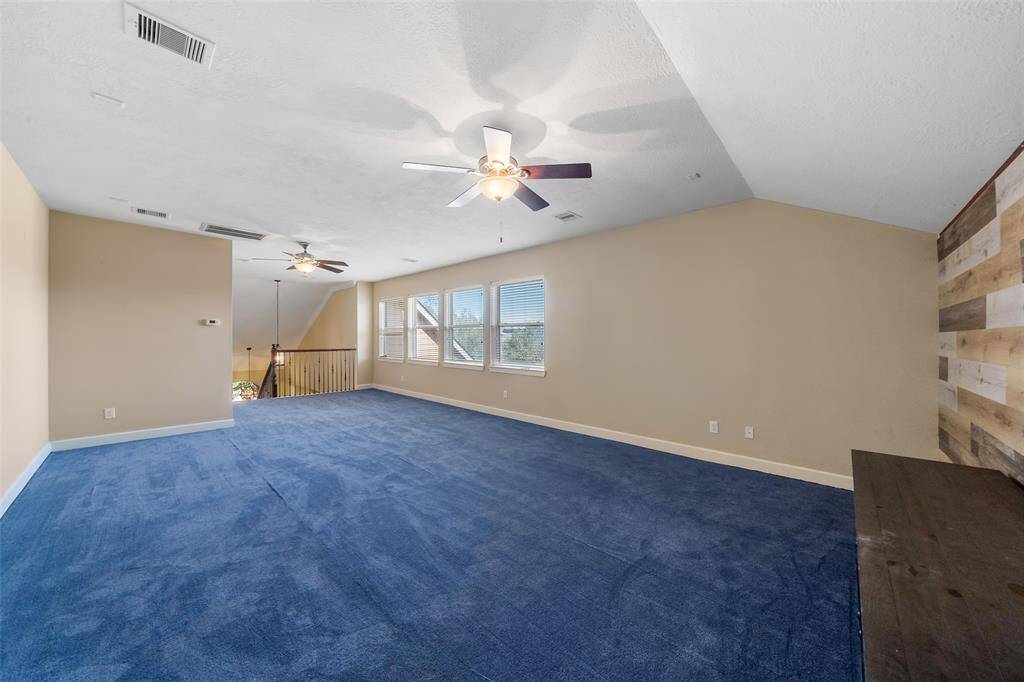 This spacious room features neutral walls with a rustic wood accent wall. It has two ceiling fans for comfort and ample natural light from a row of windows, making it versatile for various uses.