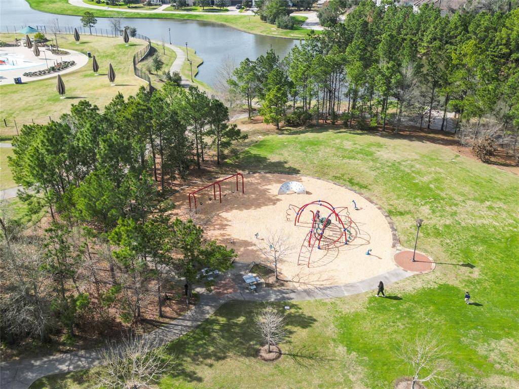 A scenic neighborhood park with a playground featuring swings and climbing structures. It's surrounded by lush greenery and near a serene water body, offering a family-friendly environment perfect for outdoor activities and relaxation.