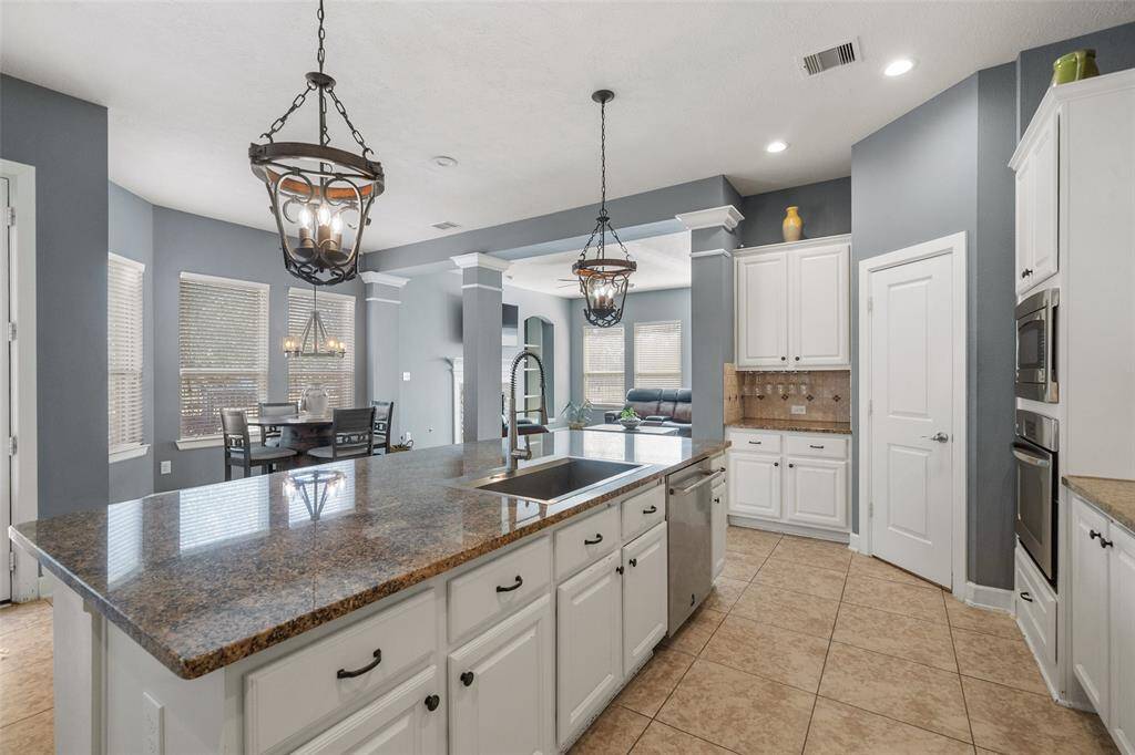 This spacious kitchen features a large island with granite countertops, stainless steel appliances, and ample cabinetry. The open layout connects to a dining area with elegant pendant lighting and abundant natural light, ideal for entertaining.