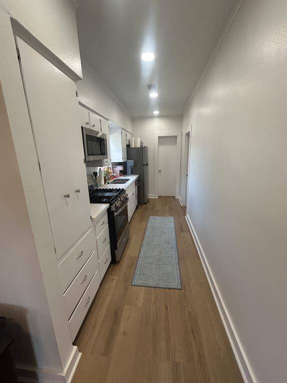 Looking from the living/dining room through the kitchen. Bathroom door in the background. Cabinets on the left, followed by the gas range with microwave, double sink, dishwasher and refrigerator.