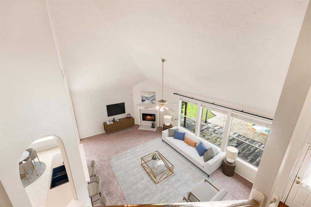 A bright and inviting living space with soaring ceilings, a cozy fireplace, and expansive windows that bring the outdoors in. *Virtually Staged