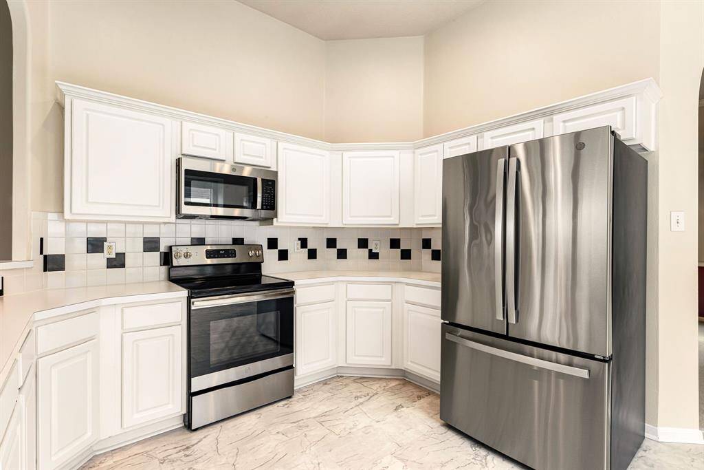 This stylish kitchen boasts crisp white cabinetry, a sleek black and white tile backsplash, and modern stainless steel appliances. The spacious layout provides ample storage and counter space, perfect for both cooking and entertaining. With its contemporary design and clean lines, this kitchen is a blend of elegance and functionality.