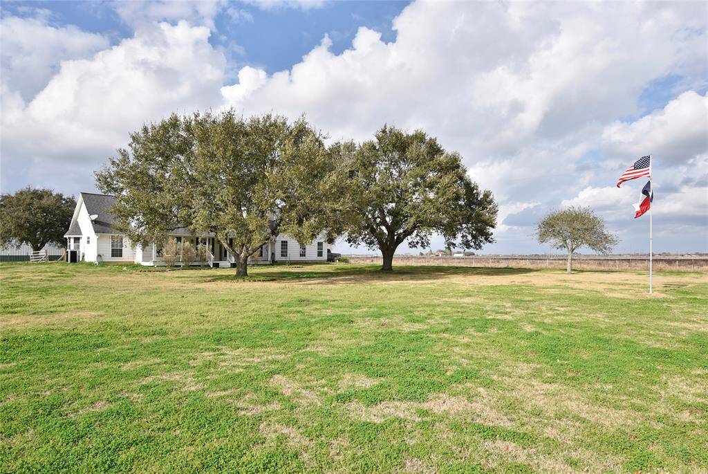Charming countryside home with a spacious lawn, mature trees, and a welcoming front porch. The expansive yard includes flagpoles, offering a serene rural setting.