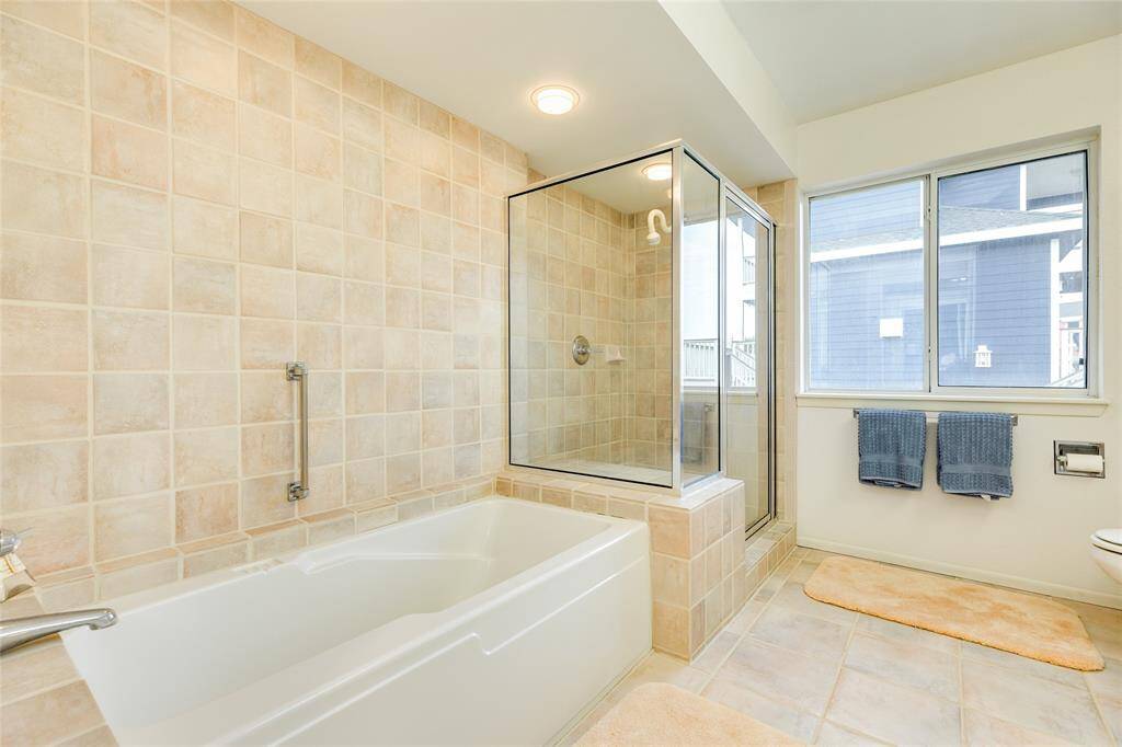 As we continue through this grand Primary en-suite. You notice the large soaking tub and separate, walk-in shower shower. This room offers the commode and and another sink with storage area.