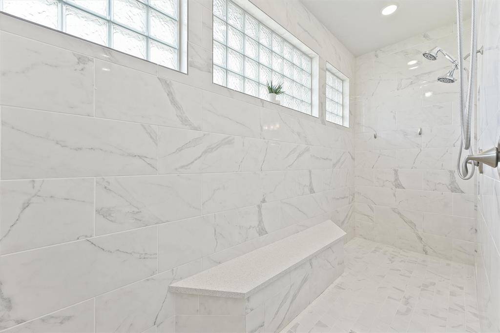 Elegant shower with marble-style tiles and glass block windows, offering plenty of natural light. It features dual showerheads and a built-in bench for added comfort and luxury.