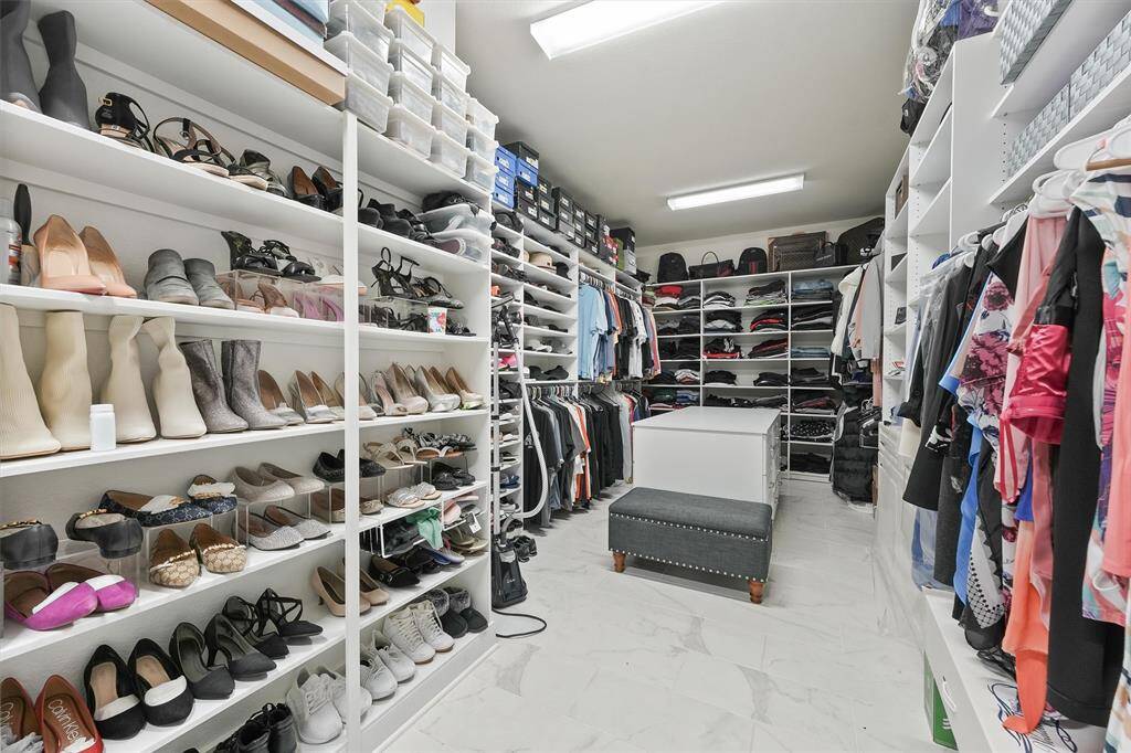 Walk-in closet with ample shelving for shoes and clothes, and a central island for additional storage. The bright lighting and tiled floor enhance the space's functionality and appeal.