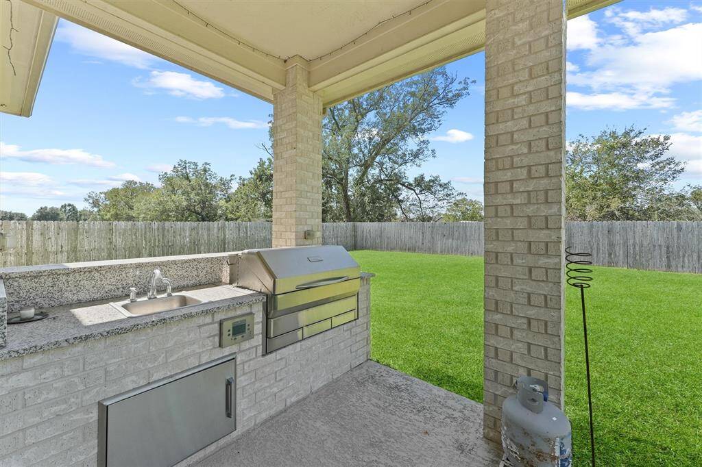 Spacious backyard with a well-equipped outdoor kitchen, featuring a built-in grill and sink, set against a backdrop of lush green grass and a privacy fence, perfect for entertaining and enjoying outdoor living.