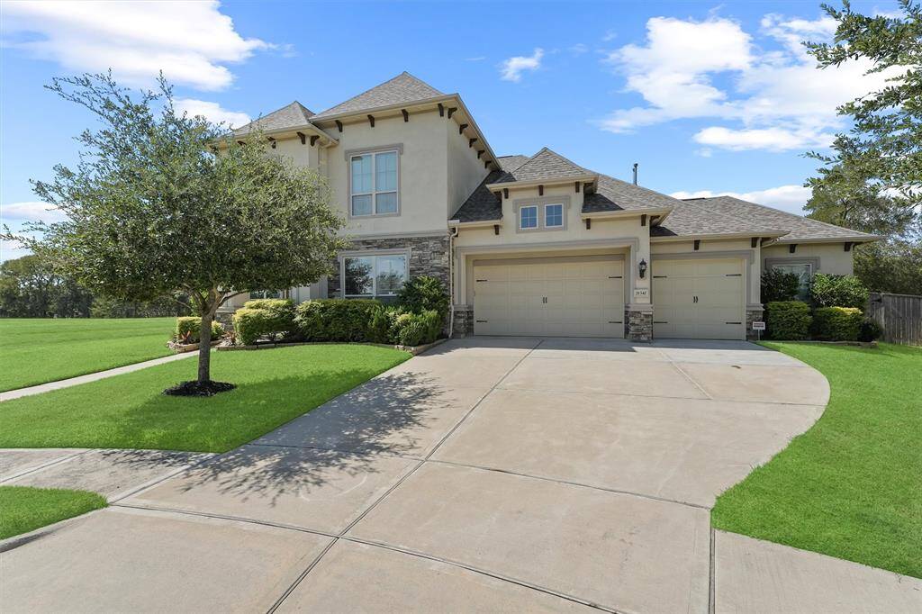 This beautiful two-story home features a spacious three-car garage and a well-maintained front yard with lush greenery and a tree. The light-colored exterior, accented with stone, offers a welcoming curb appeal, and the expansive driveway provides ample parking space.