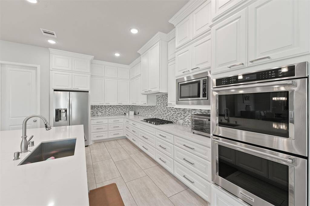 Modern kitchen with sleek white cabinetry and stainless steel appliances, including a double oven and refrigerator. Features a spacious countertop with a built-in sink and a stylish backsplash. Ideal for cooking and entertaining.
