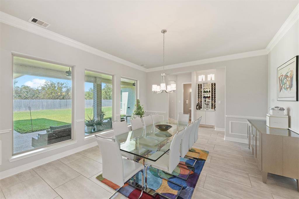 This spacious dining room features large windows offering plenty of natural light and views of the backyard. The room also has a built-in wine rack, neutral walls, and tiled flooring, creating a contemporary and inviting atmosphere.